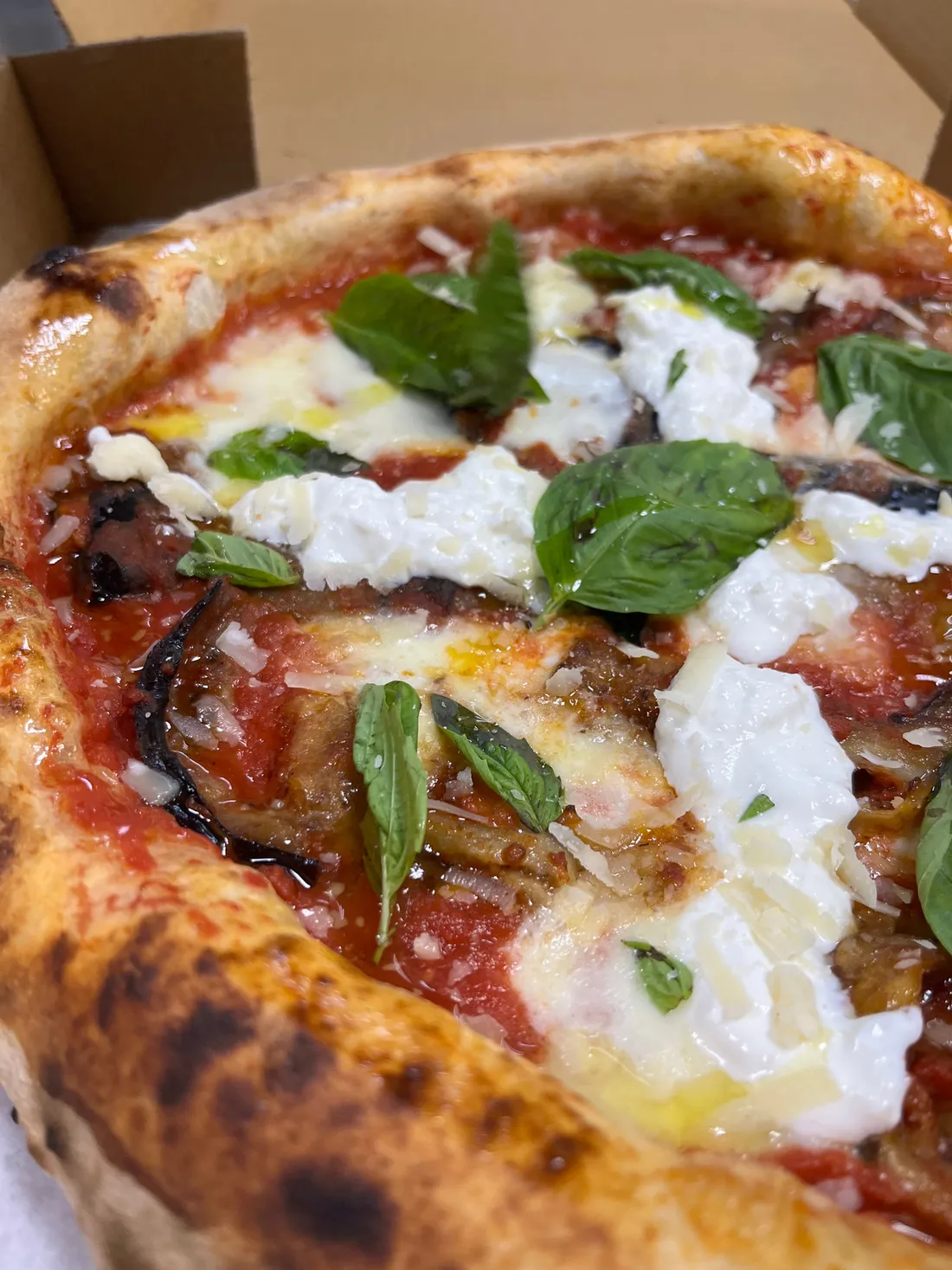 Close-up of a Neapolitan pizza with burrata, basil and eggplant