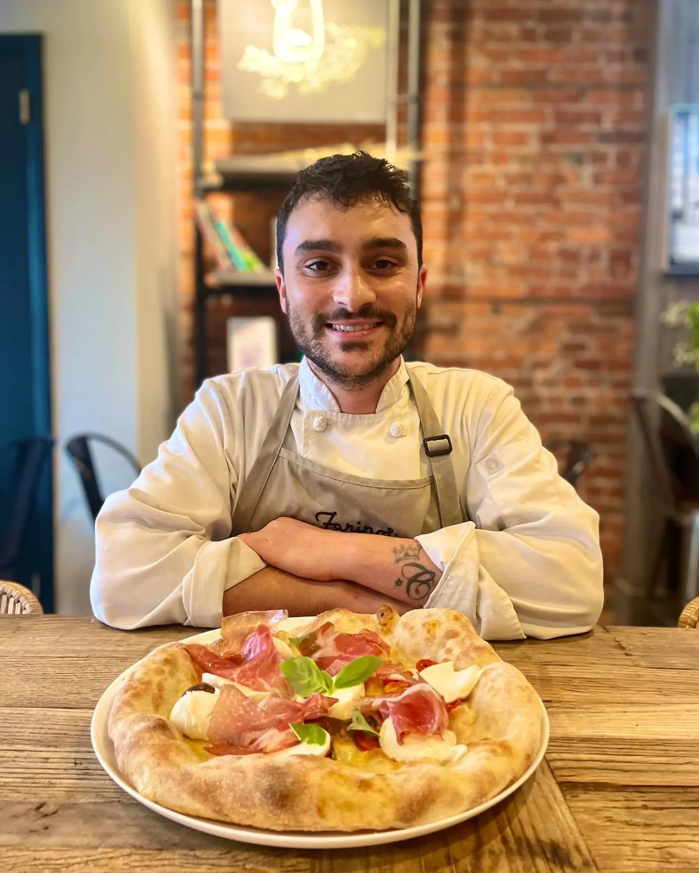 A Culto Italiano chef at a table in the restaurant with a prosciutto and mozzarella pizza
