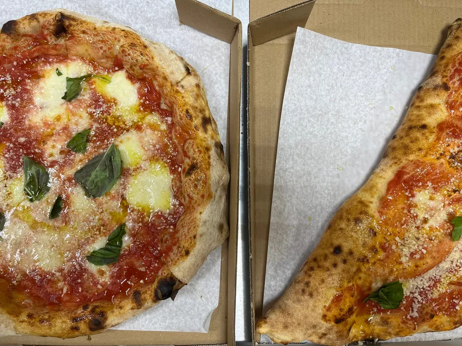 A Margherita pizza and a calzone in takeout boxes