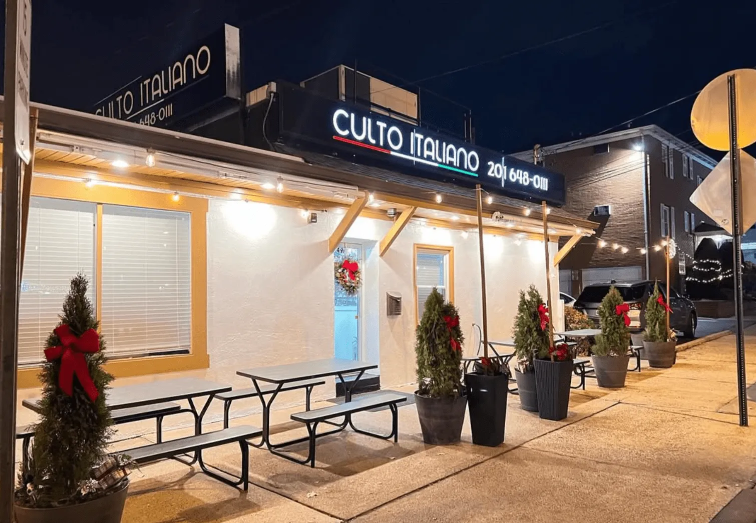 The Culto Italiano storefront at night, with string lights and holiday trees by the door