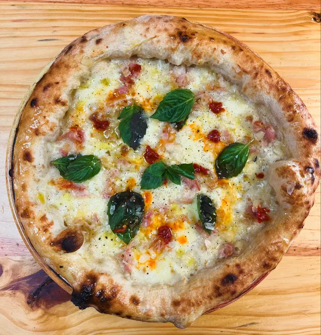 A white-base pizza with pancetta, basil and a hot honey drizzle